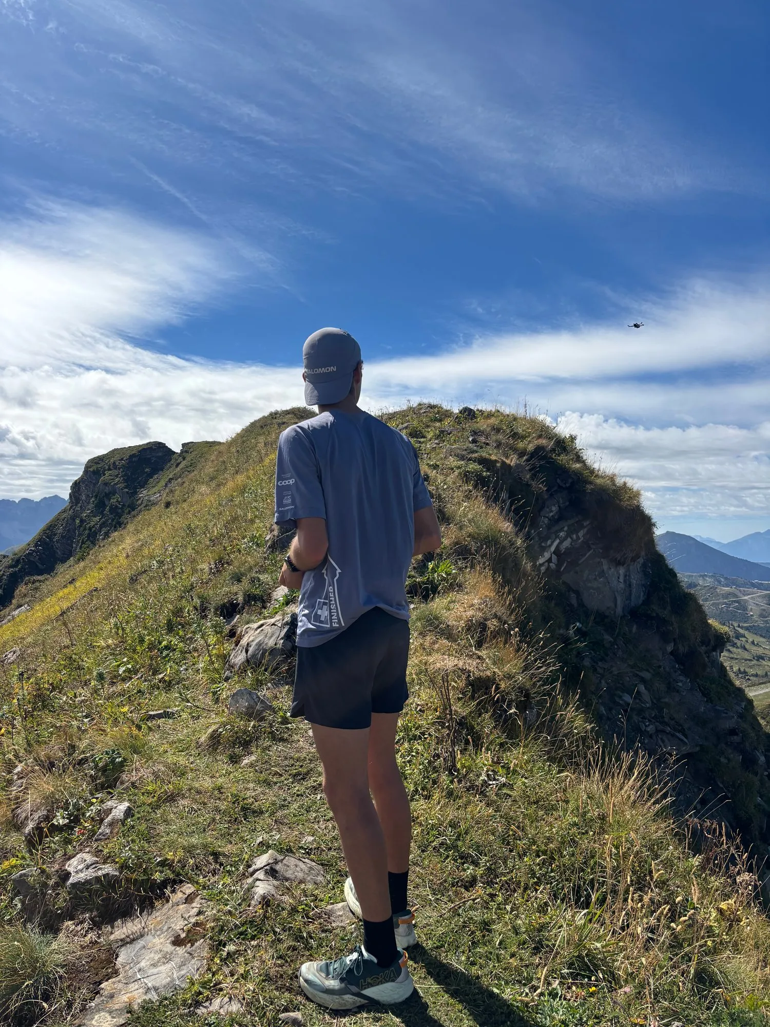 Nicolas Goullet de Rugy de dos sur une crête herbeuse à Châtel, Hoka Speedgoat 7 aux pieds